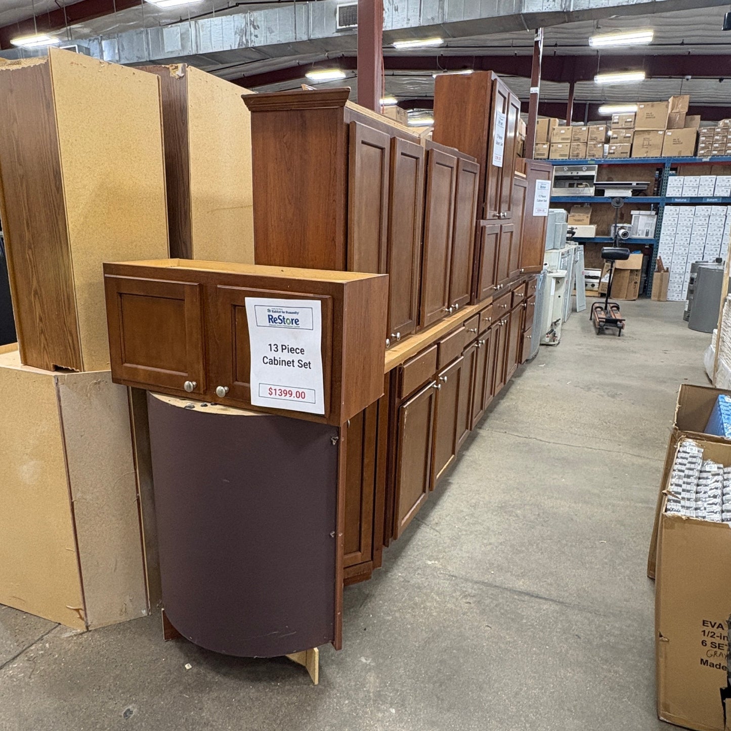 GDM Habitat for Humanity ReStore 13-piece brown wooden kitchen cabinet set displayed in a warehouse showroom.