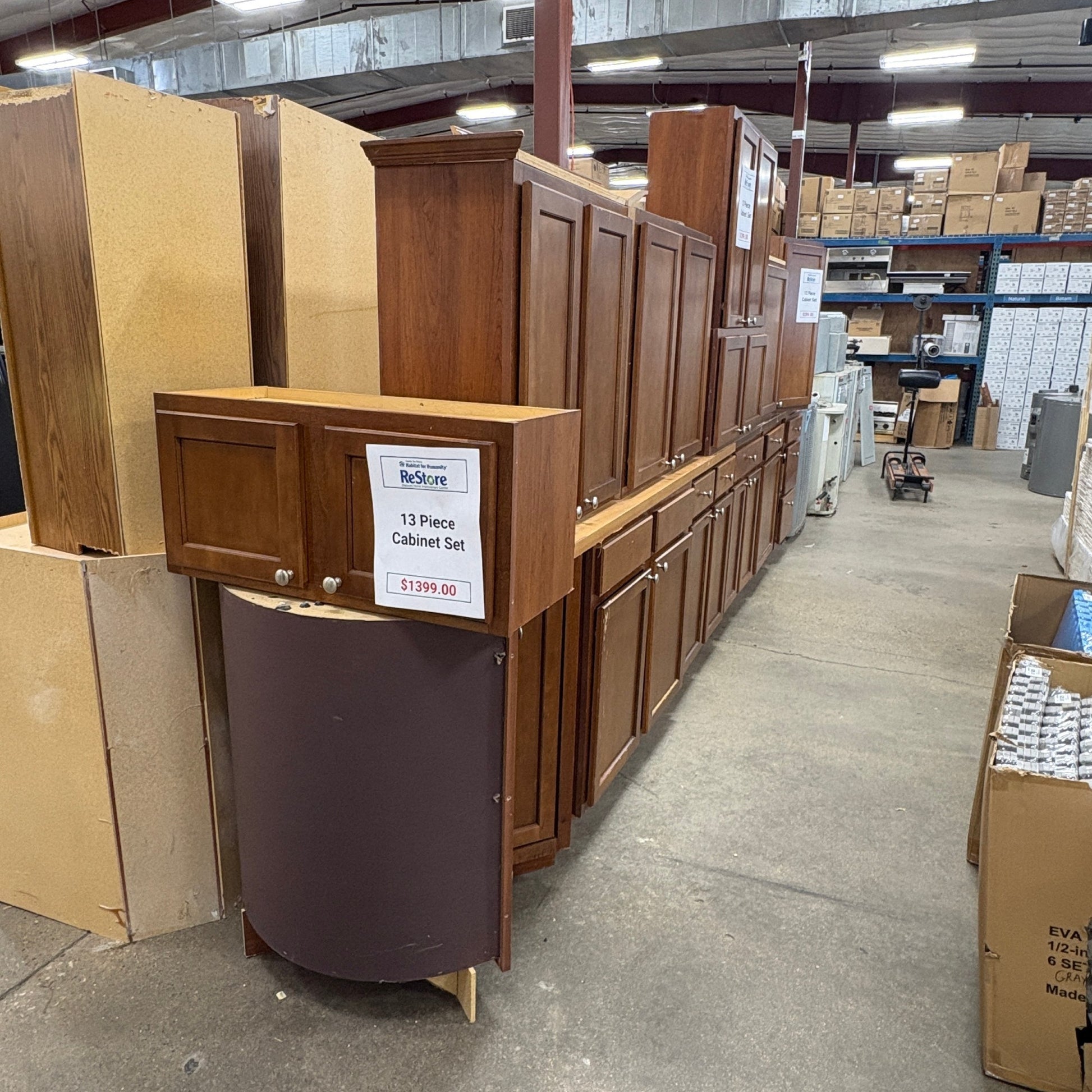 GDM Habitat for Humanity ReStore 13-piece brown wooden kitchen cabinet set displayed in a warehouse showroom.