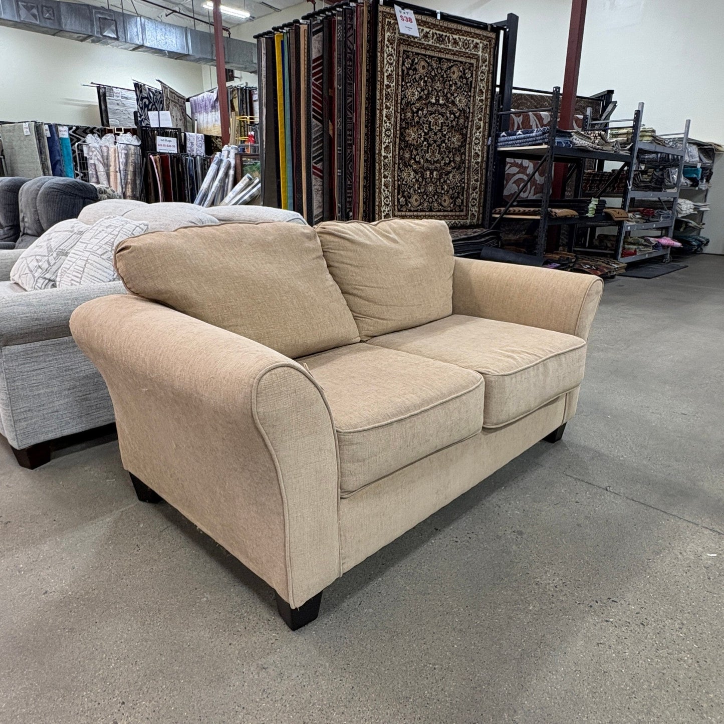 GDM Habitat for Humanity ReStore tan chenille loveseat with rolled arms and dark wooden feet in a retail showroom.