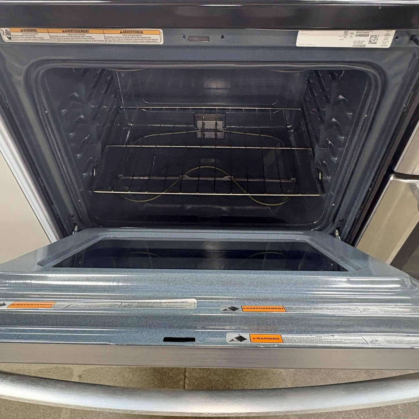 Open oven cavity of a GDM Habitat for Humanity ReStore Whirlpool electric range with a stainless steel door handle.